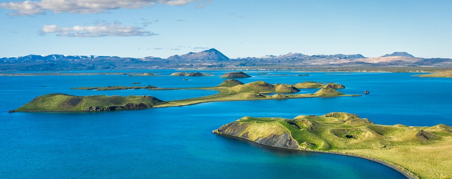 Aerial view of Lake Mývatn in North Iceland with volcanic islets, clear blue water, and distant mountains in summer