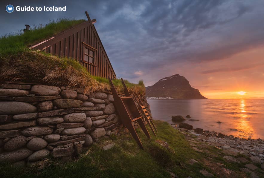 Traditional turf house in Bolungarvík, Westfjords of Iceland, at sunset with ocean view and mountain in the background