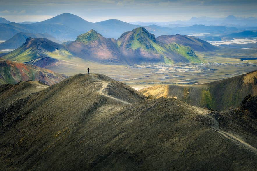 Hiker standing on a mountain ridge in Landmannalaugar, Icelandic Highlands, with colorful rhyolite mountains in summer