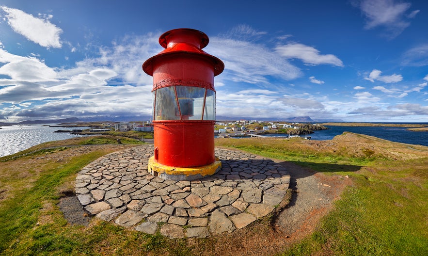 Red lighthouse in Stykkisholmur overlooking Breidafjordur bay under a bright blue sky with scattered clouds.