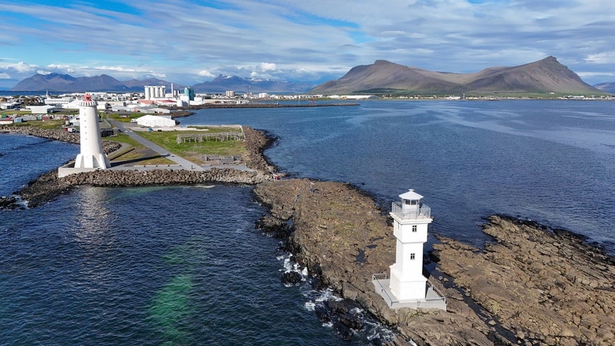 Twin lighthouses in Akranes, Iceland—Akranesviti Old and New—stand on rocky shores with mountains and town in the background.
