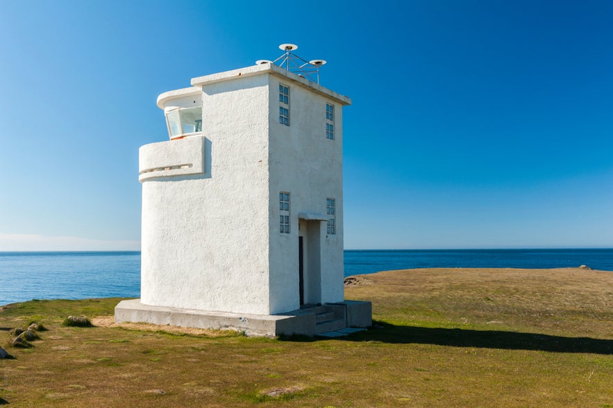Bjargtangar Lighthouse, Iceland’s westernmost lighthouse, stands on grassy cliffs overlooking the ocean under a clear blue sky.