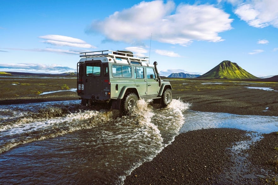 4x4 crossing a river in the Highlands while driving in Iceland in August near Landmannalaugar and volcanic mountains.