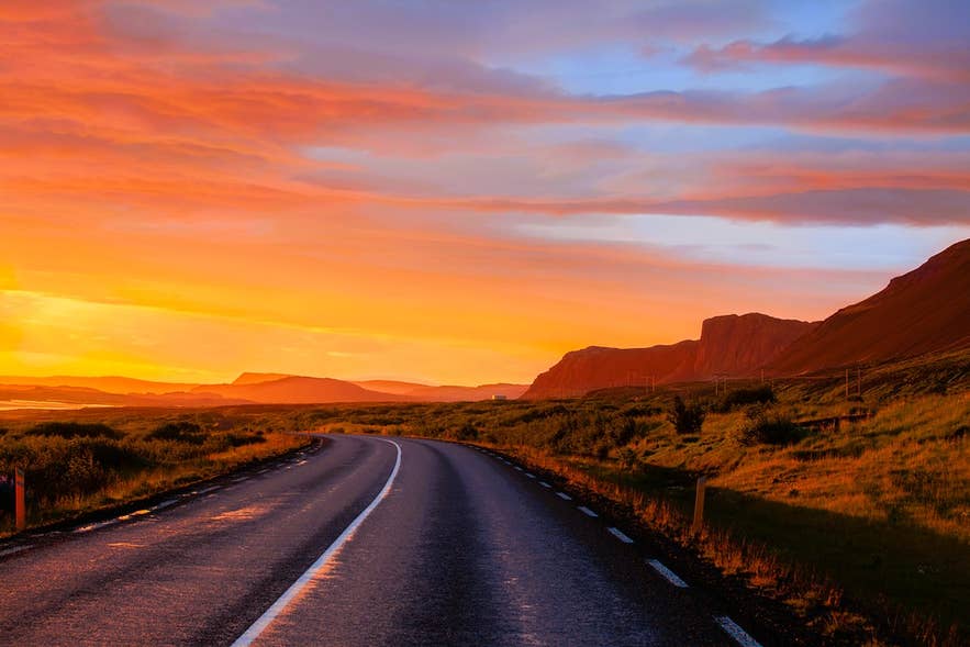 Golden sunset light over a quiet Icelandic highway on a long summer evening.