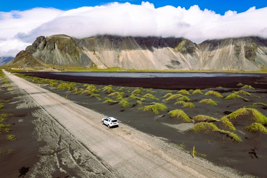 White car on a gravel road near Vestrahorn with black sand dunes in Southeast Iceland.