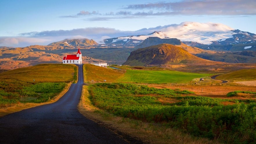 Iconic red-roof church at sunrise with glacier backdrop seen while driving in Iceland in August on Snaefellsnes.
