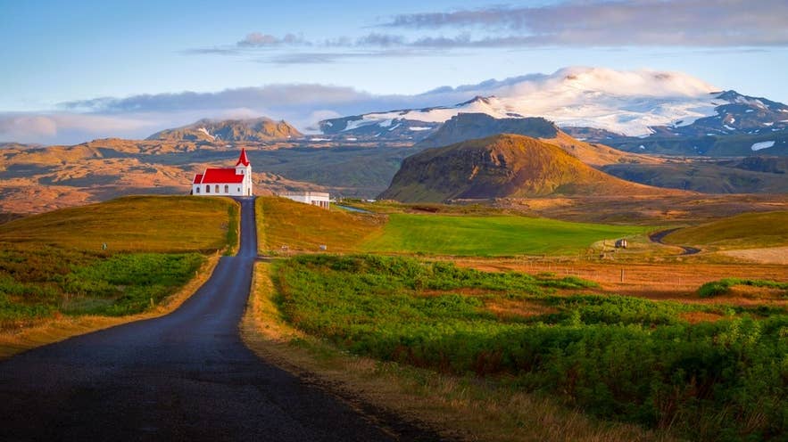 Red-roof church at sunrise with a glacier rising behind it on the Snaefellsnes Peninsula.
