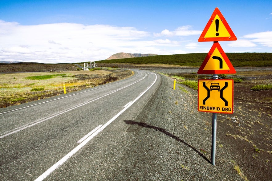 Sharp turn and narrow bridge warning signs spotted while driving in Iceland in August near a Highland route.