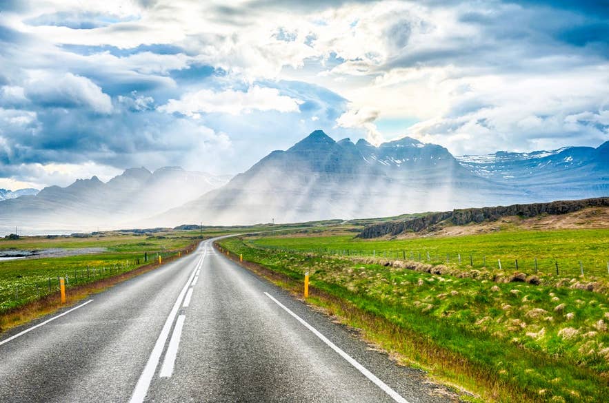 Straight paved road stretching toward misty mountains in East Iceland under long summer daylight.