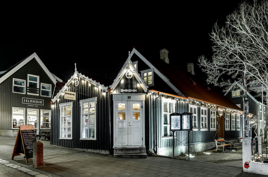Traditional black wooden house lit at night, home to BakaBaka restaurant in downtown Reykjavík.