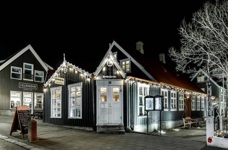 Traditional black wooden house lit at night, home to BakaBaka restaurant in downtown Reykjavik.