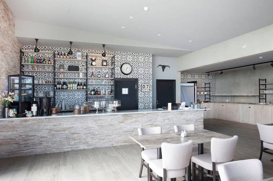 Modern cafe with a stone counter, patterned tile backsplash, and shelves stocked with wine, liquor, and glassware.