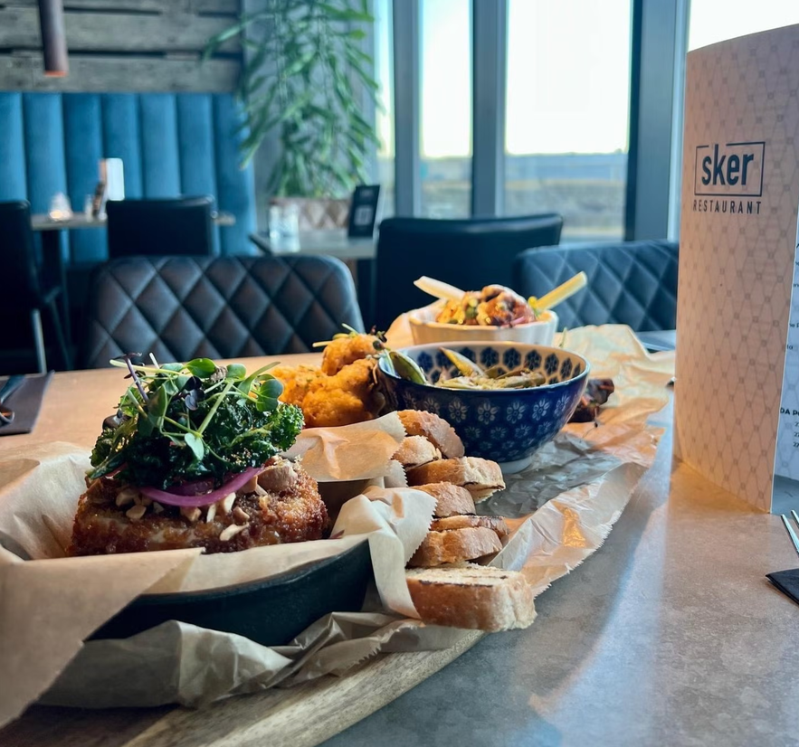 Forskellige gourmetforretter på et træbræt på Sker Restaurant, bl.a. brødskiver, salat, kroketter og en velsmagende tærte.