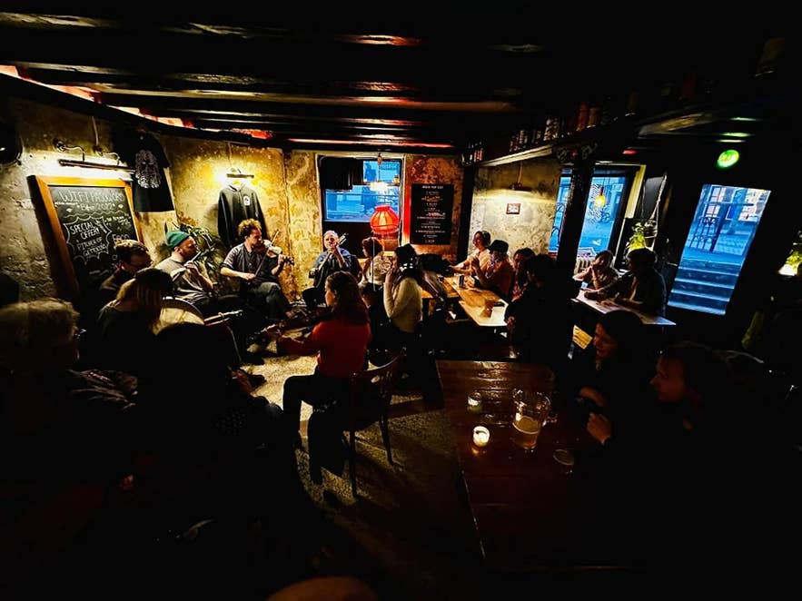 Gezellige pub met sfeervolle verlichting, een live folkband met violen en fluiten, en gasten dicht bijeen rond houten tafels.