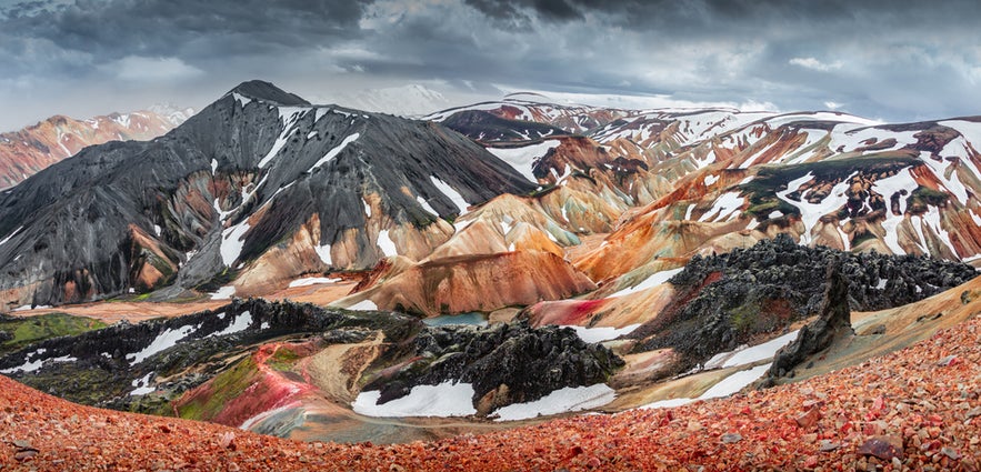 Colorful rhyolite peaks of the Landmannalaugar Mountains in Iceland, with patches of snow and dramatic clouds overhead.