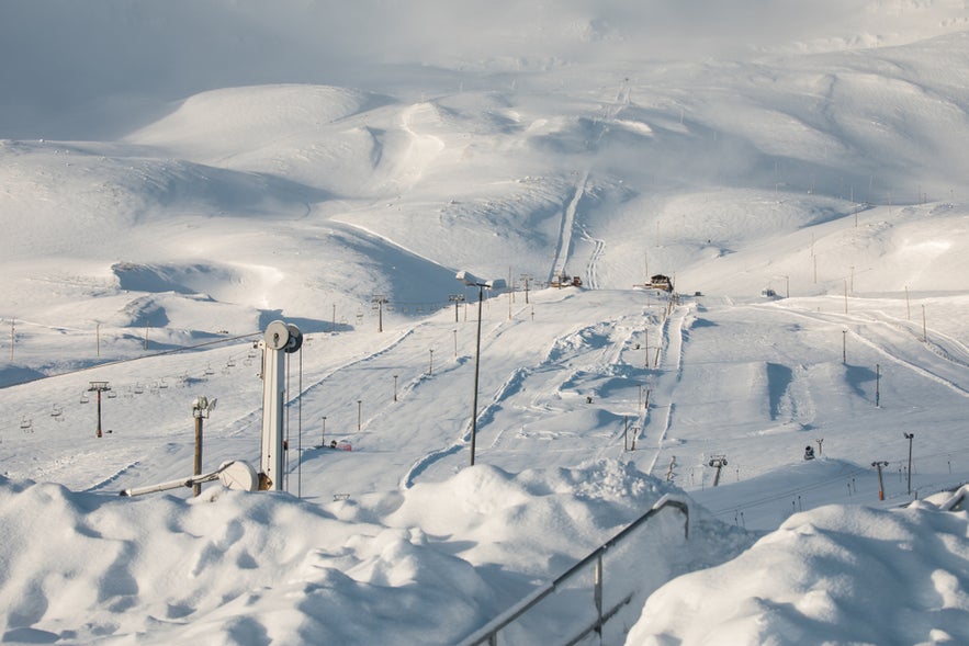 Snow-covered Hlidarfjall Mountain ski resort with chairlifts, groomed slopes, and snowy hills under a soft winter sky.
