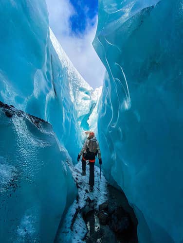 Un viajero camina por el Laberinto de Grietas en el glaciar de Skaftafell, rodeado de paredes de hielo azul resplandeciente.