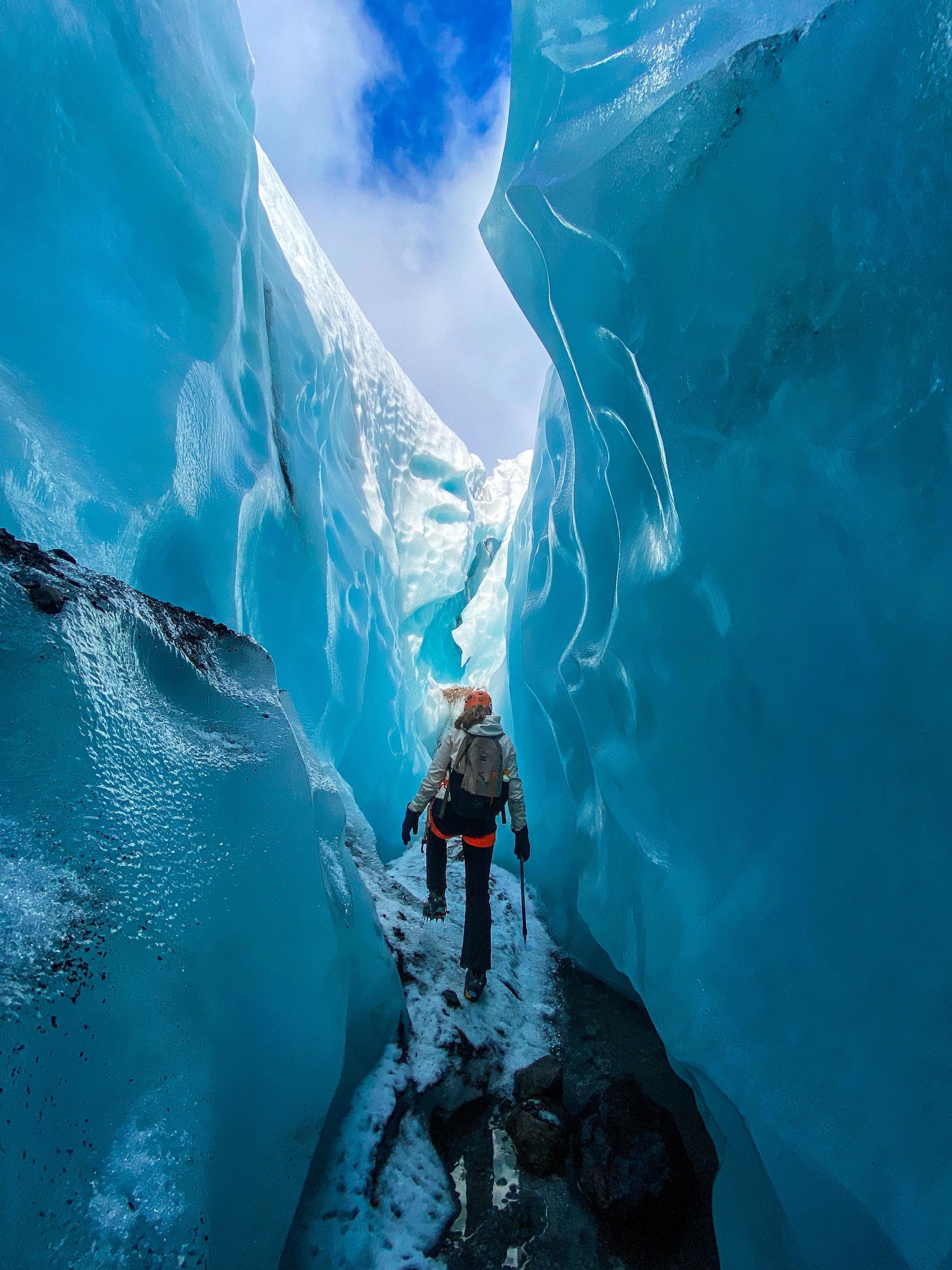 Un viajero camina por el Laberinto de Grietas en el glaciar de Skaftafell, rodeado de paredes de hielo azul resplandeciente.