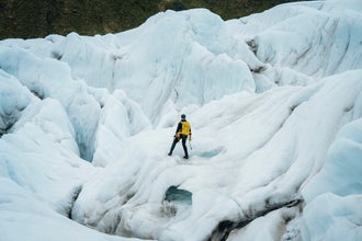A hiker with a yellow backpack stands on the glacier, overlooking rugged ice formations on the Skaftafell glacier tour.