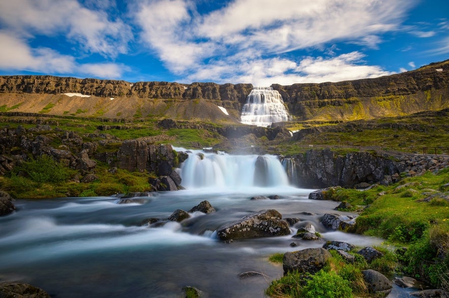 Majestic Dynjandi waterfall cascades down tiered cliffs in Iceland’s Westfjords, with lush greenery and flowing river below.