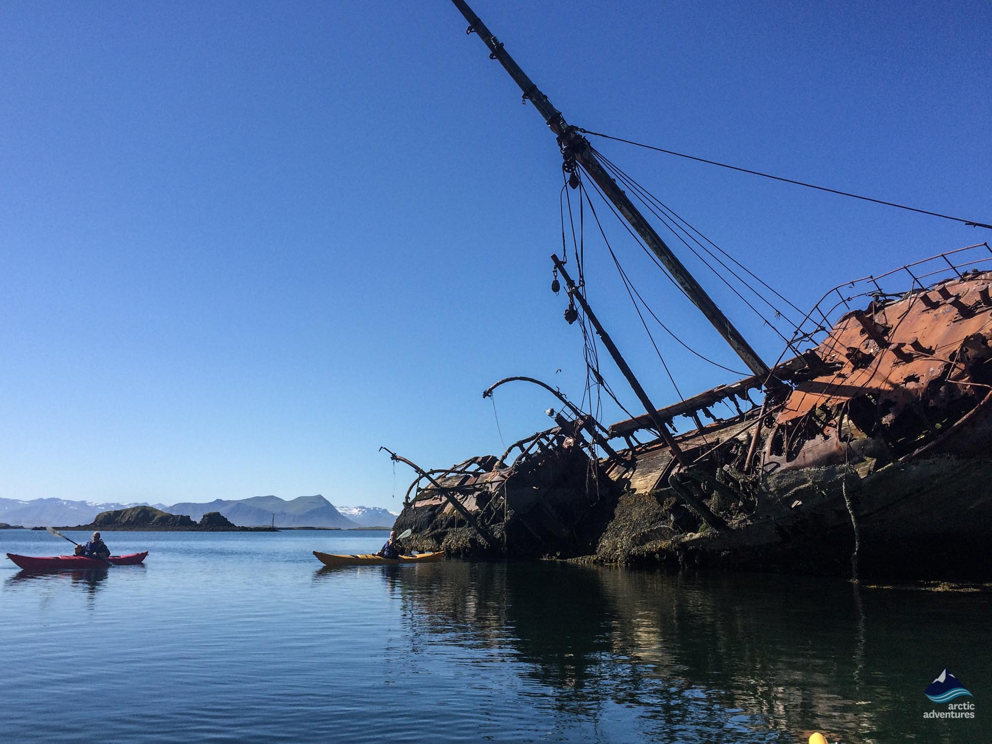 Stykkisholmur Shipwreck with kayakers paddling near the rusted remains on a clear day.
