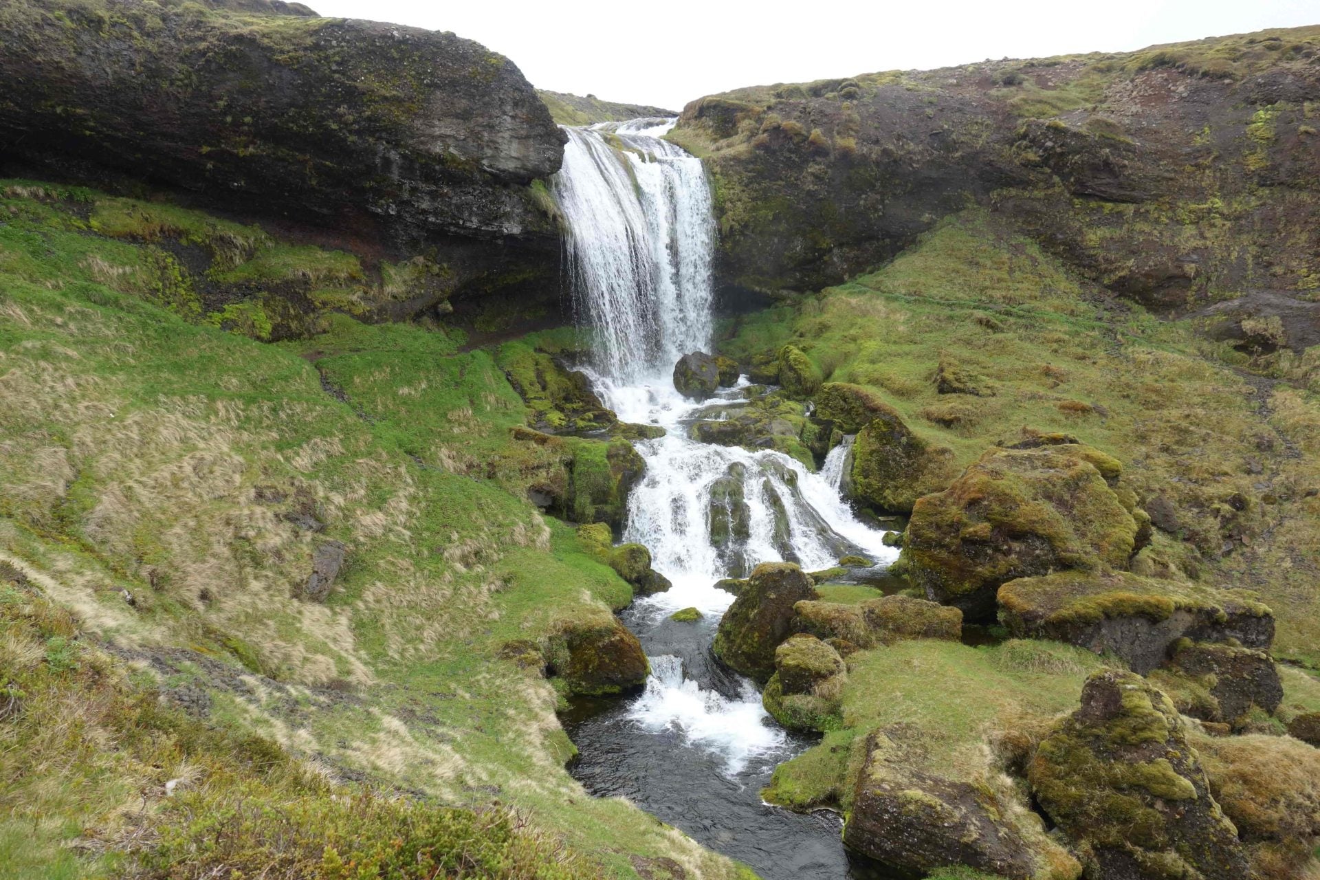 Selvallafoss Waterfall cascading over mossy cliffs surrounded by green hills.