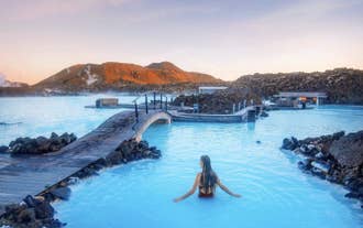 Woman relaxing in the warm waters of the Blue Lagoon with mountains and lava fields in the background.