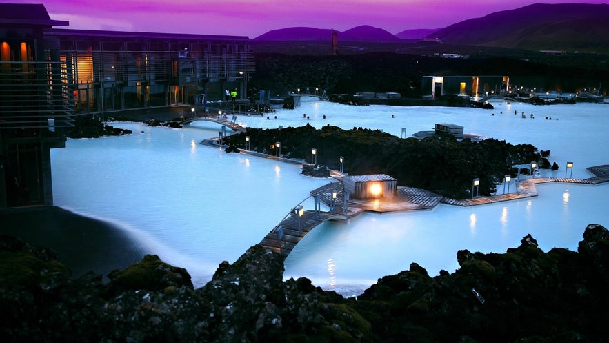 Blue Lagoon geothermal spa in Iceland at dusk, with glowing blue water, lava rock surroundings, and purple evening sky