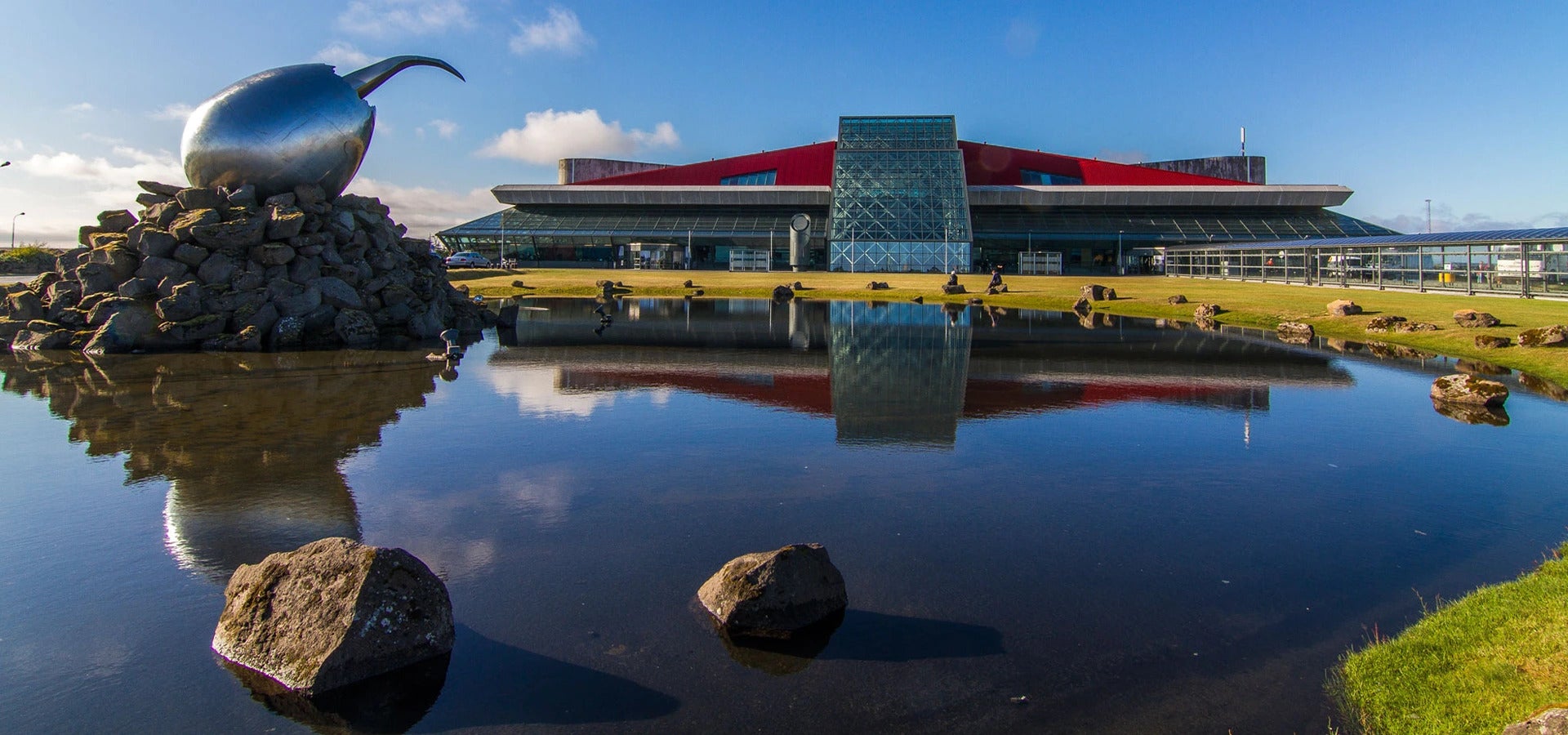 Keflavik International Airport reflected on calm water under a bright blue sky.