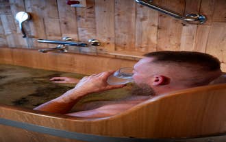 Guest enjoying a relaxing beer bath at Blabjorg Resort while sipping a refreshing drink in a wooden tub.