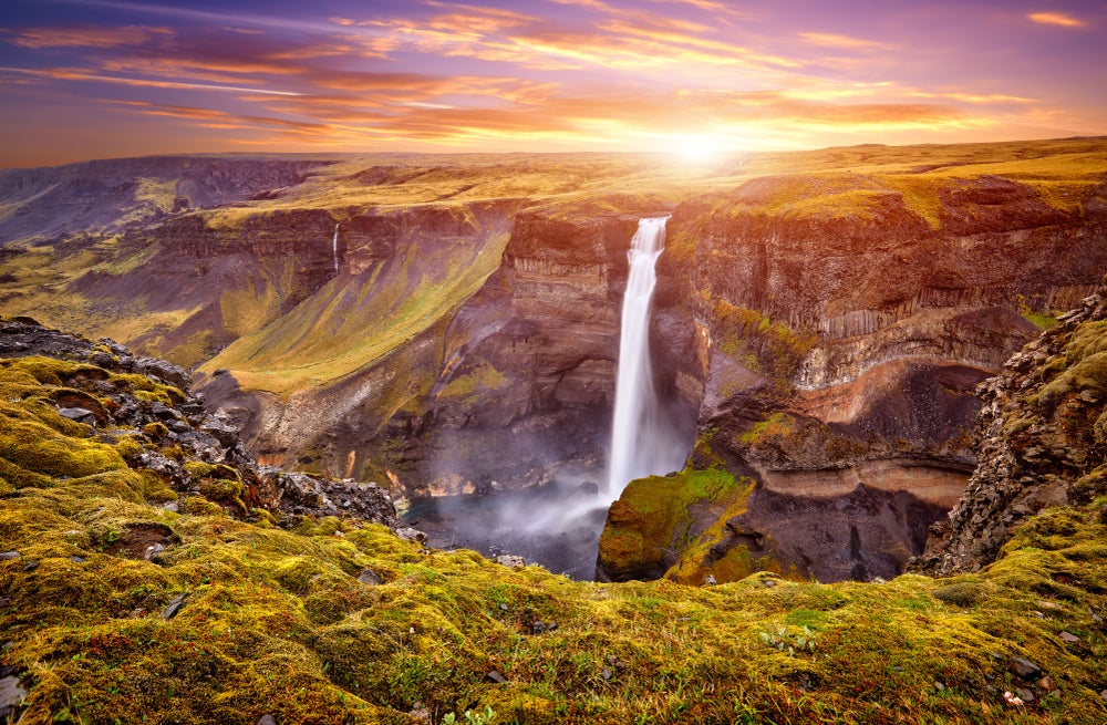 Haifoss Waterfall cascades into a deep canyon surrounded by mossy cliffs under a vibrant sunset sky in Iceland.