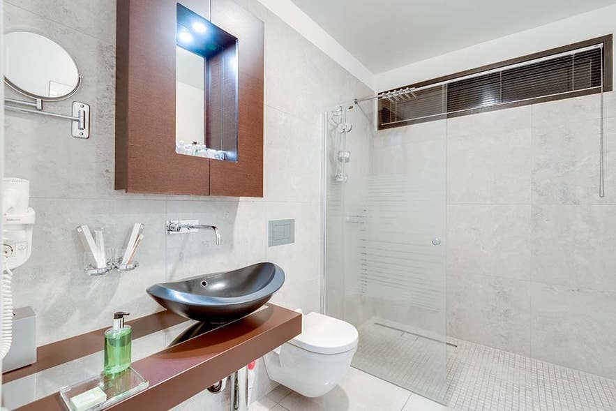 Das Badezimmer der Standard Suite im Black Pearl in Reykjavik mit großer Dusche, WC, Waschbecken und Spiegeln.