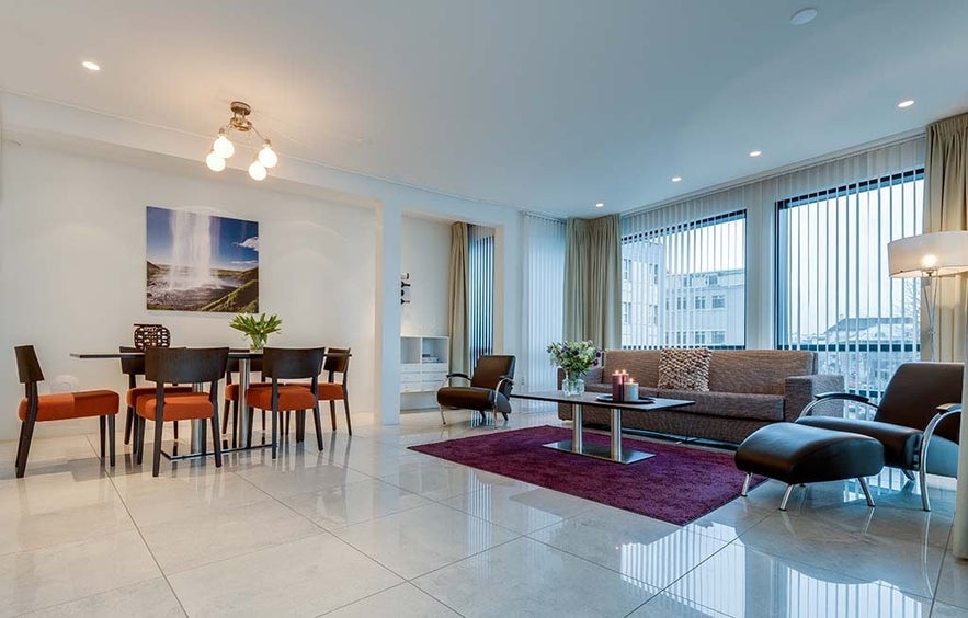 A spacious living and dining area in the Deluxe Suite at the Black Pearl in Reykjavik, which has a dining table and chairs, a couch, and large windows.