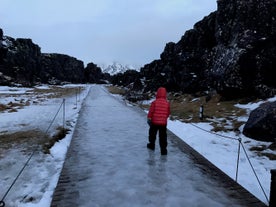 A person walks along an icy wooden walkway in the Thingvellir National Park.