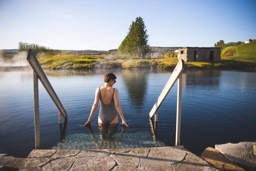 Bezoeker betreedt de Secret Lagoon (Gamla Laugin) in Fludir, Zuid-IJsland, met geothermische stoom en historische omgeving.