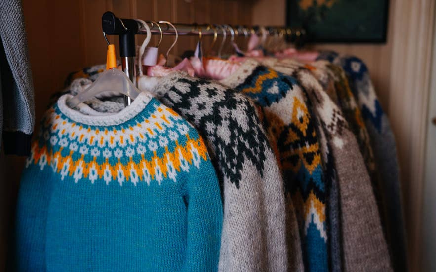 Bunte Woll-Lopapeysa-Pullover auf einer Stange, die traditionelle isländische Strickmuster zeigen.