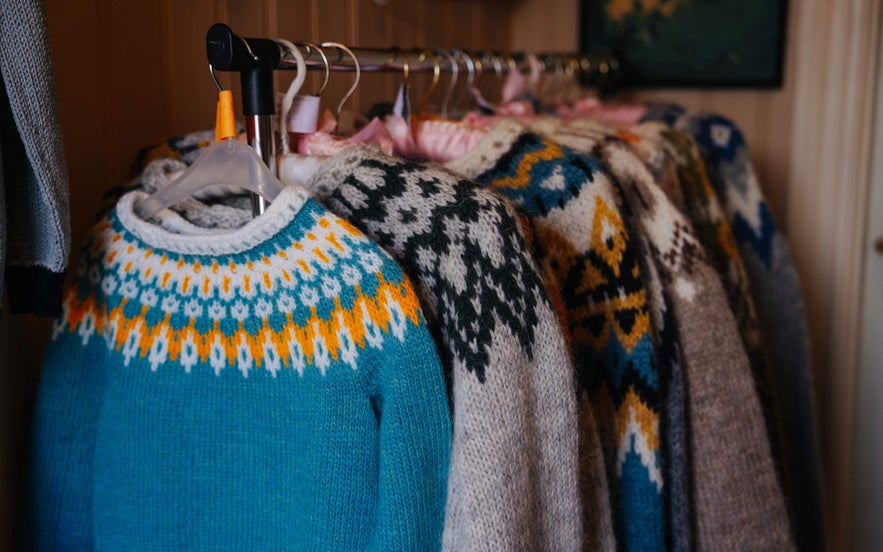 Colorful wool lopapeysa sweaters hanging on a rack, showcasing traditional Icelandic knitting patterns.