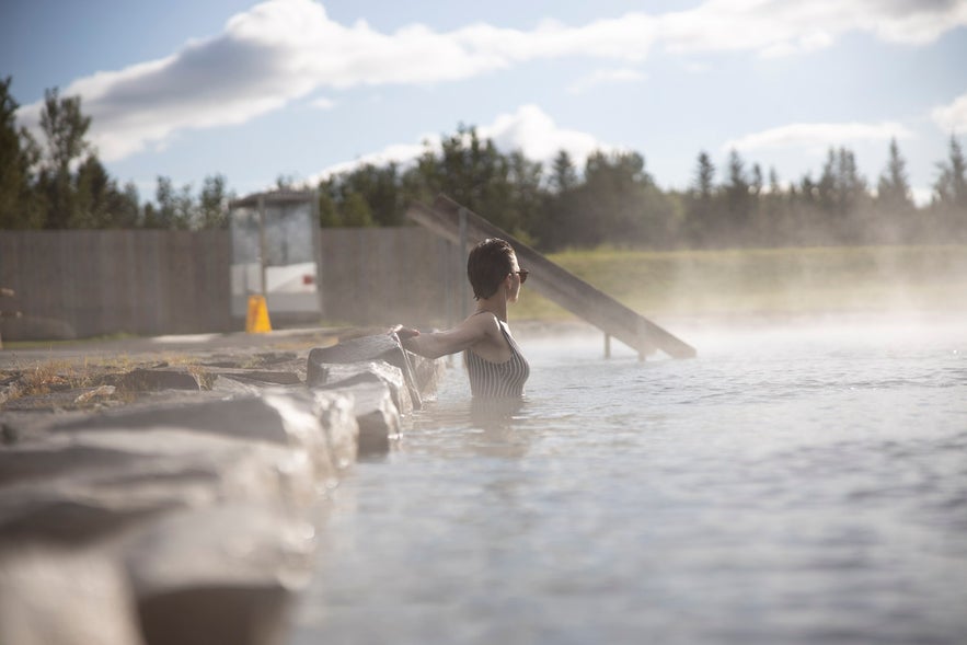 Steam rises and surrounds a woman who is taking a bath in the Secret Lagoon.