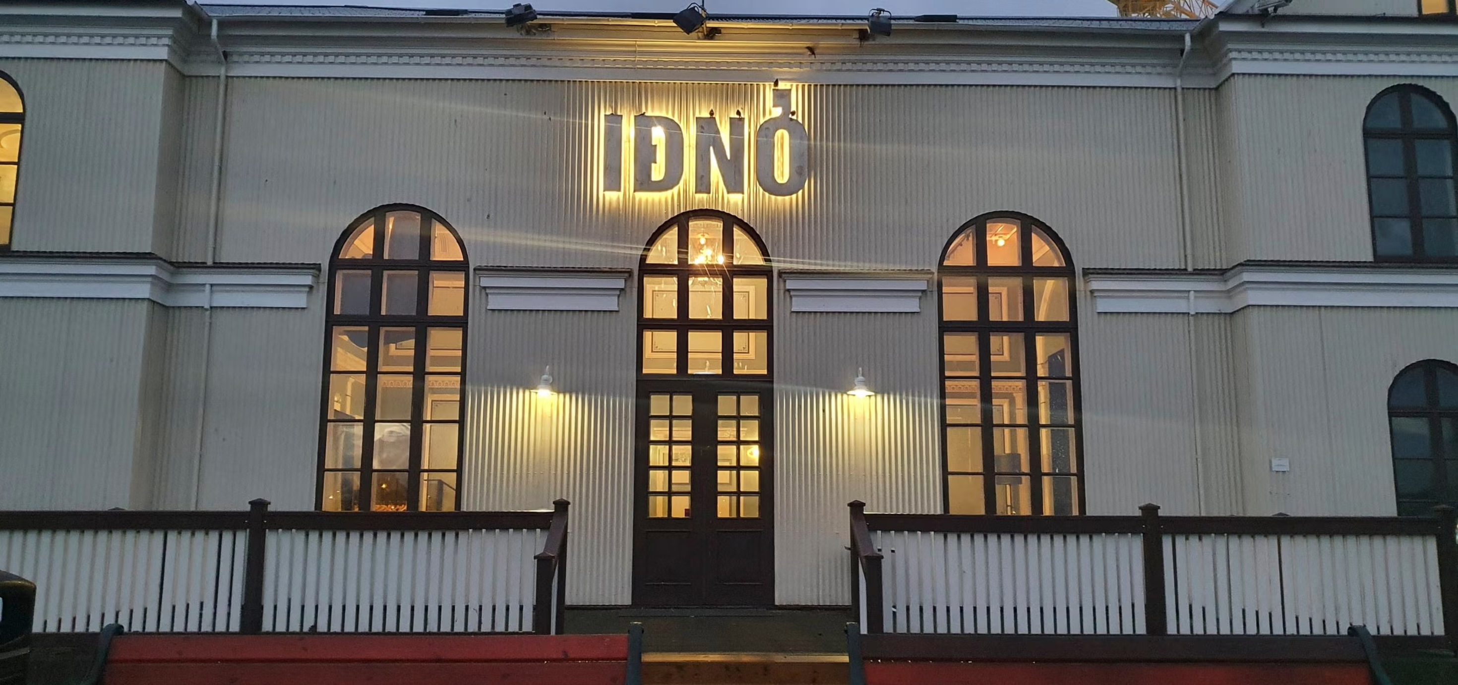 Den historiska IDNO-byggnaden i Reykjavik på Island, upplyst i skymningen med varmt ljus från höga välvda fönster.