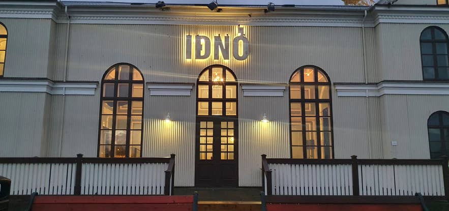 The historic IDNO building in Reykjavik, Iceland, illuminated at dusk with warm lights glowing through tall arched windows.