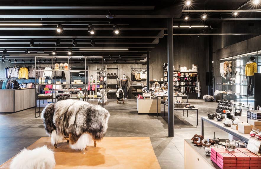 Moderner isländischer Designladen mit fellbedeckten Hockern, Kleiderständern, Accessoires und Geschenkartikeln, präsentiert unter hellen Spots.