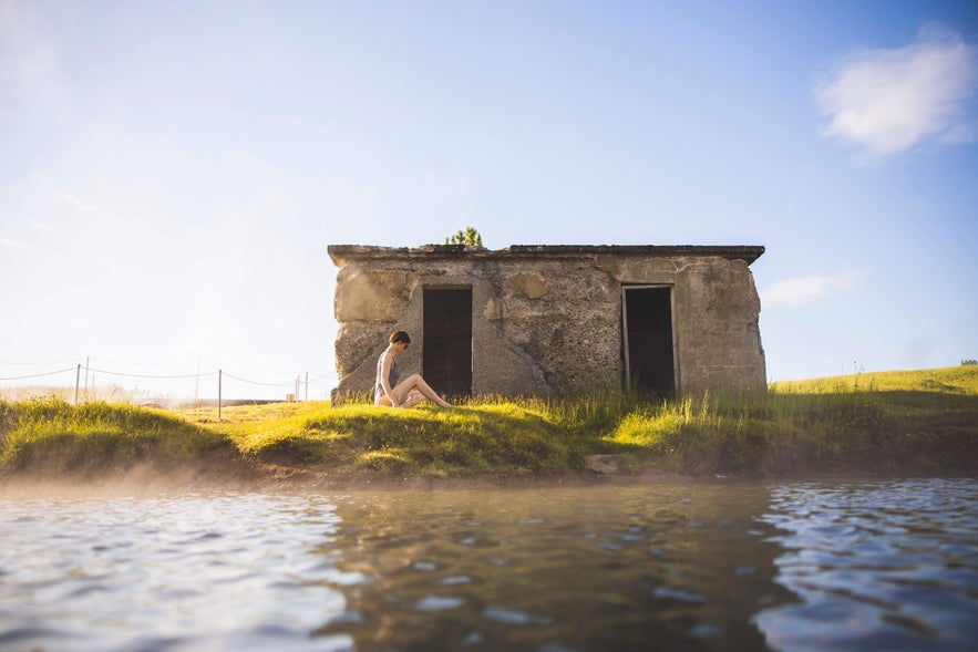 A woman sits peacefully on the grass in front of the old building at the Secret Lagoon.