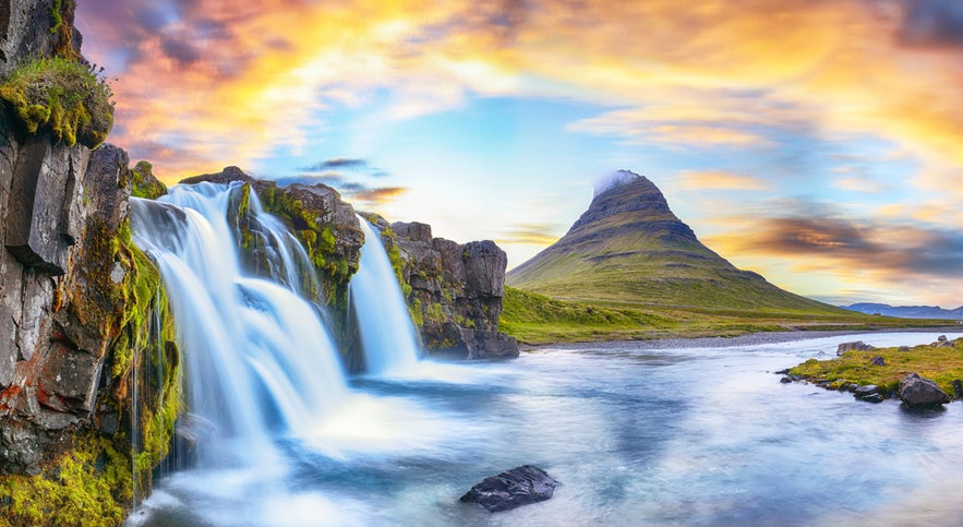 Kirkjufellsfoss Waterfall flowing beside the iconic Kirkjufell mountain in Iceland under a colorful, dramatic sunset sky.