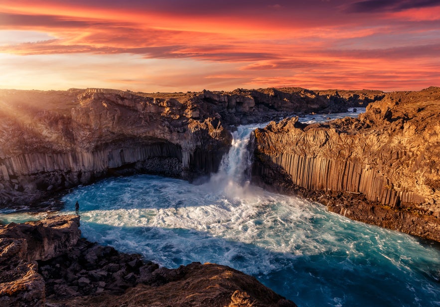 Aldeyjarfoss Waterfall pouring through basalt columns into a blue pool under a vibrant sunset sky in Iceland.