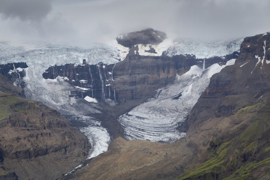 Morsarfoss Waterfall cascading from a glacier over steep cliffs in Iceland, surrounded by ice, rock, and cloudy skies.
