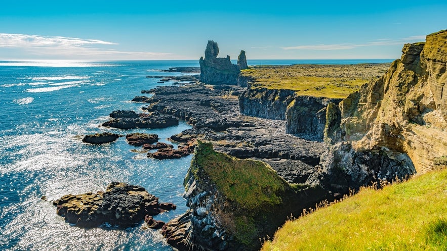 Rugged sea cliffs near Hellnar on the Snæfellsnes Peninsula, Iceland, with lava rocks and shimmering ocean waters.