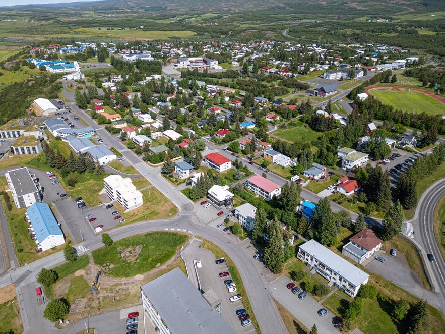 Aerial view of Egilsstaðir, a small town in East Iceland with colorful houses, green trees, and surrounding hills.