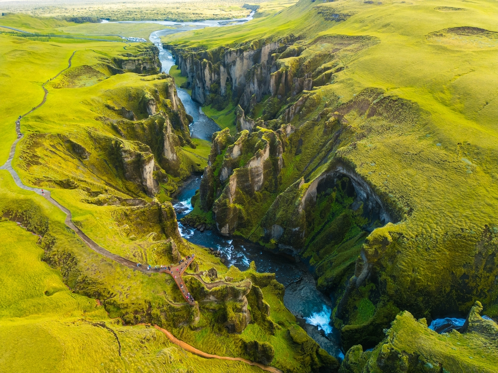Aerial view of Fjadrargljufur canyon in Iceland, with steep green cliffs and a winding blue river below.