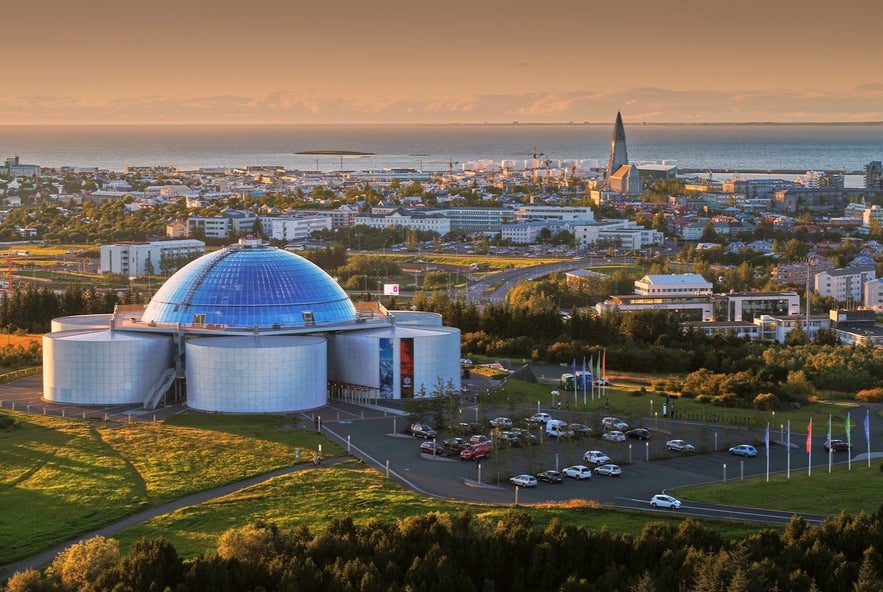 View of Perlan museum with its glass dome in Reykjavik, Iceland, overlooking the city and Hallgrímskirkja Church near the coastline at sunset.