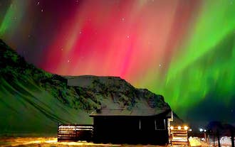 Northern lights glowing in red and green above South Iceland's Green Farm Stay cabin.